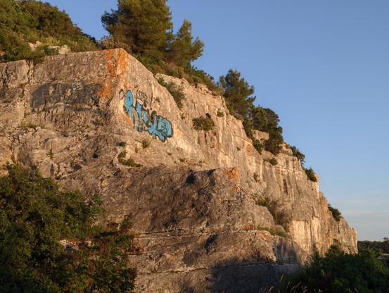 Felswand mit blauem Graffiti wird von der Abendsonne angestrahlt